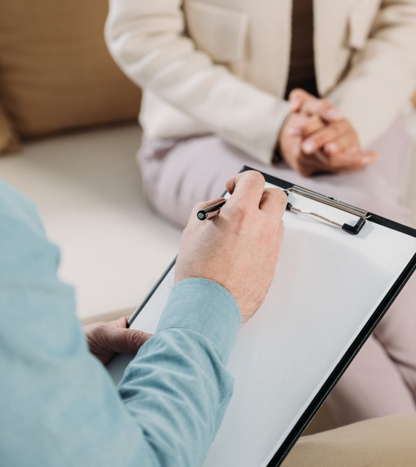 cropped-shot-of-psychotherapist-writing-on-clipboard-and-female-patient-sitting-on-couch.jpg